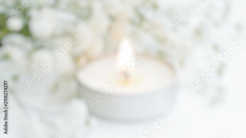 A simple yet elegant arrangement of white flowers sits next to a burning white candle