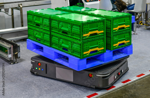 Autonomous mobile robot AMR AGV carrying blue plastic pallet with green crates in modern smart warehouse factory
