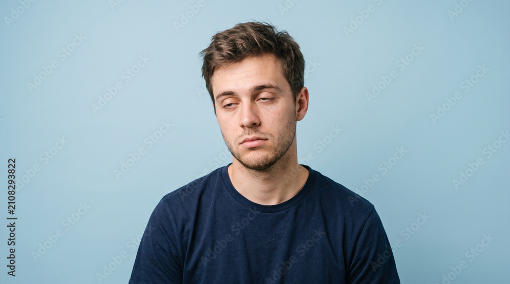 Fototapeta premium Bored Young Man Looking Down with Tired Expression Against Blue Background