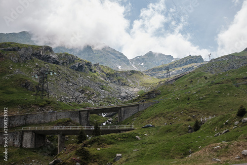 Bild auf Leinwand Majestic mountain pass with rugged green slopes and dramatic cloudy skies