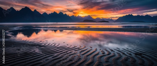 Breathtaking Sunset Over Mountain Range with Tranquil Waters Reflecting Vibrant Colors and Unique Sand Patterns in a Serene Coastal Landscape