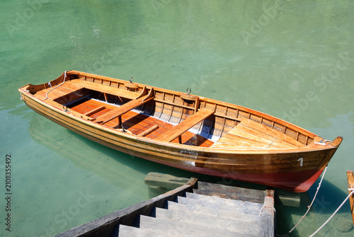 Traditional wooden rowboat moored on crystal-clear turquoise lake with dock and calm water. Peaceful outdoor scene ideal for travel, recreation, nature and summer themes.