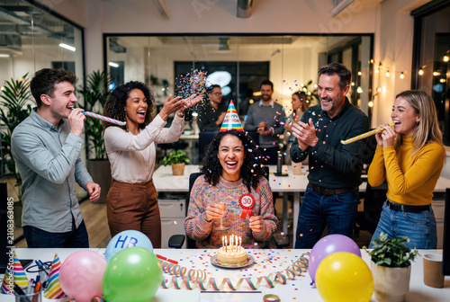 Cheerful office team celebrating a coworker birthday with confetti and party decorations inside a modern corporate workspace. Employee appreciation and positive company culture concept