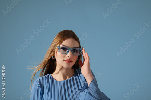 Beautiful fashionable woman wearing trendy blue color sunglasses, stylish pleated dress. Close up studio portrait. Copy, empty space for text