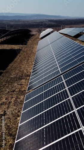 Solar panels arranged in rows on a grassy field under a clear blue sky, showcasing the renewable energy technology in a rural landscape with distant hills