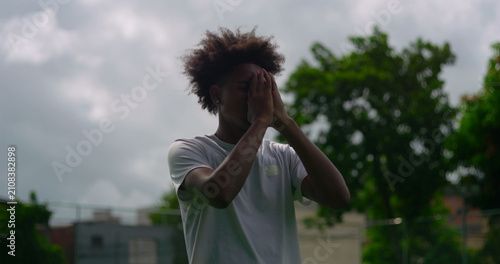 Fotografie Young African American man praying with closed eyes outdoors, showing faith, sur
