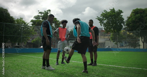Фотография Young Hispanic man kicking soccer ball during casual game with friends, losing b