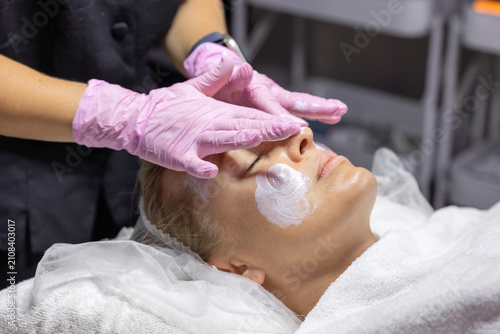Foto Cosmetologist applies protective facial cream to a client's skin after a professional skincare treatment, completing the procedure with nourishing post-treatment care