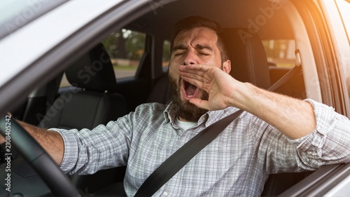 Man driving car yawning due to fatigue on road