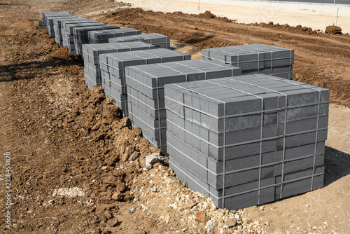Fotografie Pallets of grey concrete paving blocks stand in a row on raw dirt ground