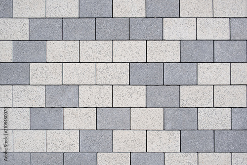 Rectangular concrete paving blocks form a clean geometric pattern. Light and dark grey stone tiles cover the walkway surface in top down