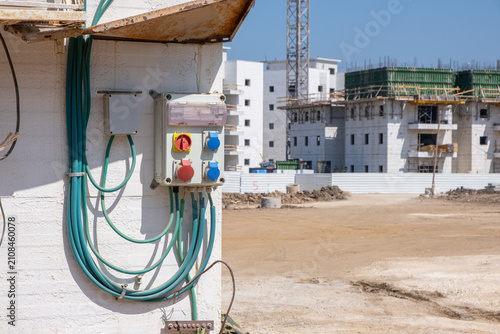temporary electrical distribution box mounted on building wall at construction site in israel. Unfinished apartment buildings stand across