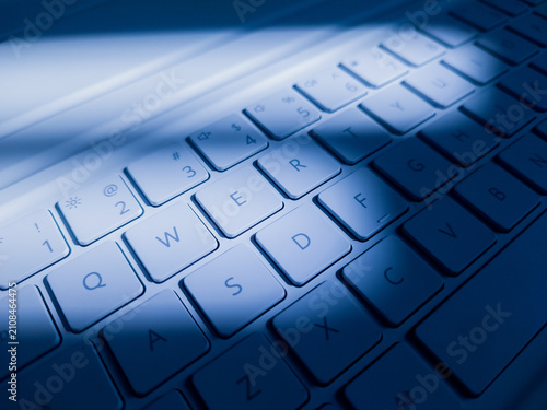 Fotografie Modern white laptop QWERTY keyboard illuminated with cool blue light and dynamic shadows, representing modern technology, computing, typing, and digital work