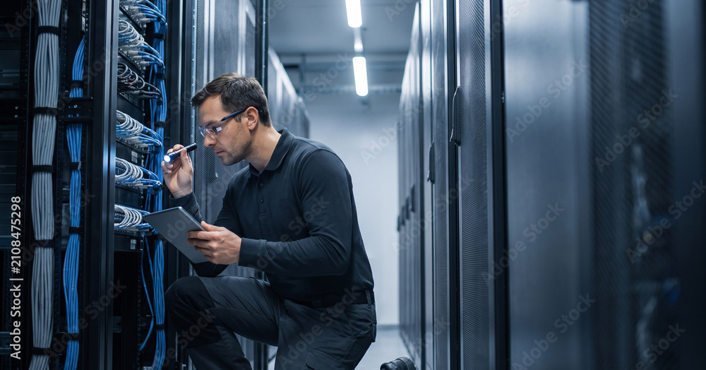 Fototapeta premium A technician is inspecting networking equipment inside a server room. He is holding a clipboard and analyzing the wires and connections.