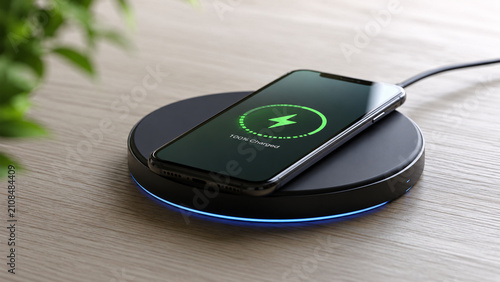 Smartphone charging wirelessly on a sleek black inductive charging pad on a wooden desk showing full battery notification concept for smart technology, fast charging, and modern workspace