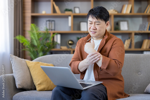 Schilderij op canvas Asian man experiencing severe wrist pain and discomfort while working on his lap