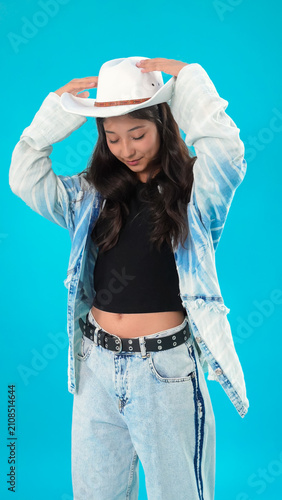 Stylish teenage girl in cowboy hat posing with hands on her head smile
