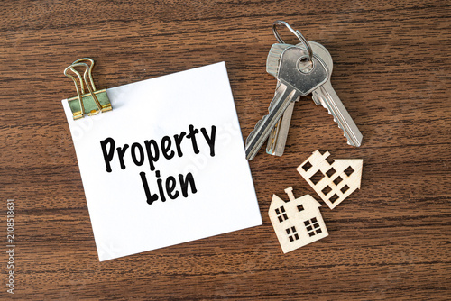 Property Lien text on white paper with keys and toy houses on wooden desk, real estate finance and law concept