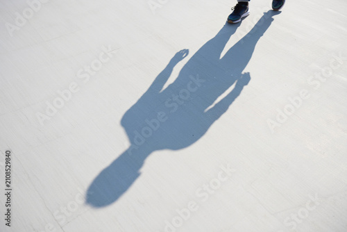 Person walking casting long shadow on white ground, legs and shoes visible