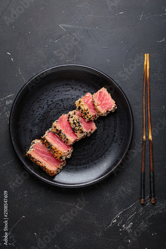 Seared grilled tuna steak tataki slices sesame seeds lemon black plate healthy delicacy