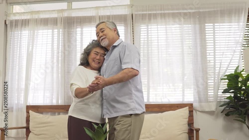 Asian senior couple embracing enjoy dancing and smiling together in the living room. Retired people do activity at home. Love and bonding of grandparents. Healthy living and insurance concept