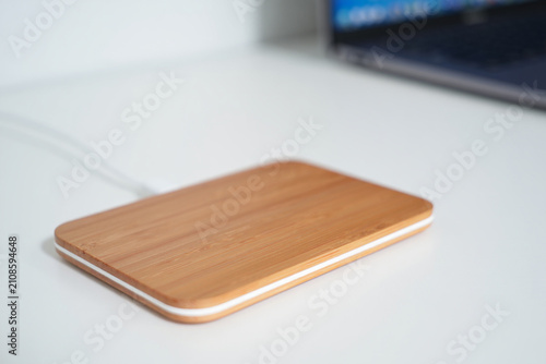 Rectangular wooden wireless charger with white trim on desk with laptop