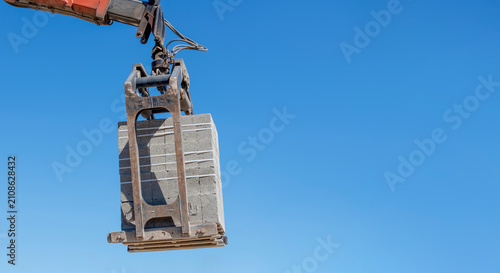 Construction crane lifts a large concrete block in clear blue sky at a building site during daytime hours