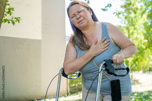 Bild auf Leinwand Middle-aged woman walking rollator leaning on walker clutching chest pained expr
