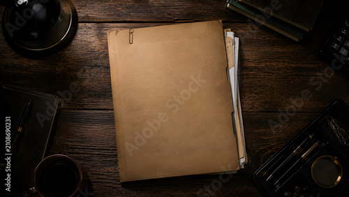 Vintage documents and office supplies arranged on a dark wooden surface featuring a paper folder and writing tools files manuscript
