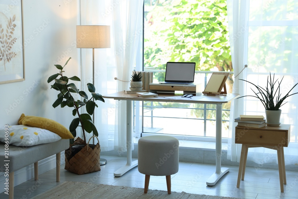 Fototapeta premium Workplace with laptop and stationery on table near window in office