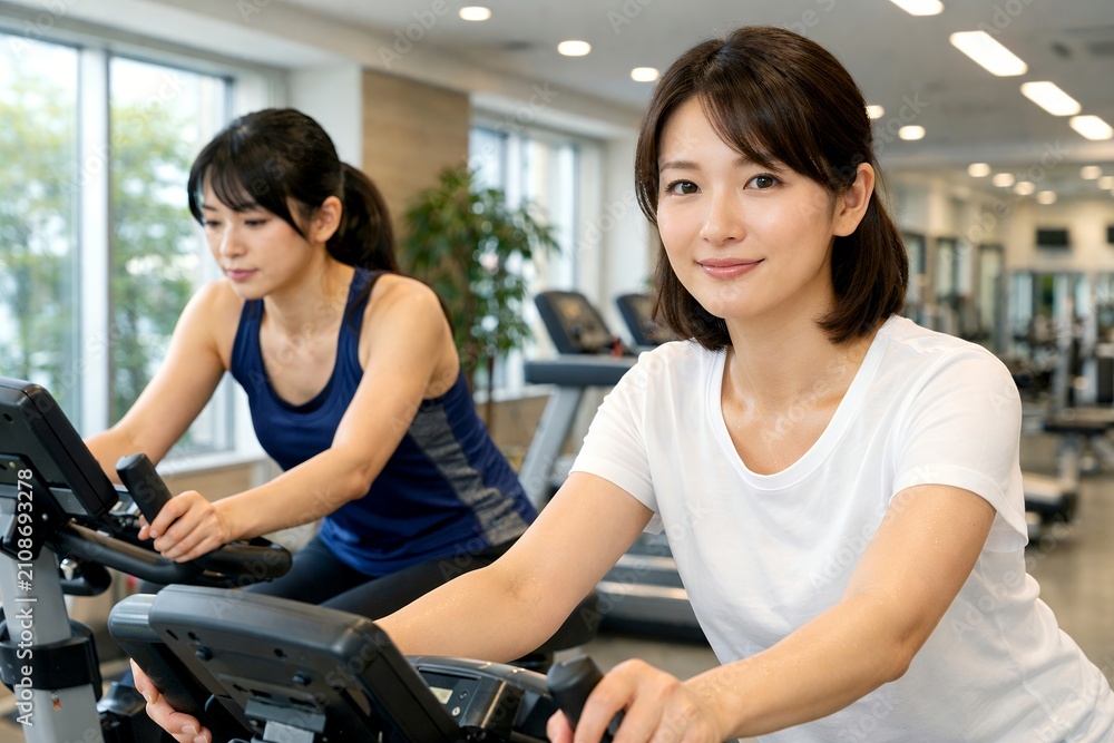 Fototapeta premium 健康的な笑顔でジムで運動フィットネスバイクを漕ぐ日本人女性