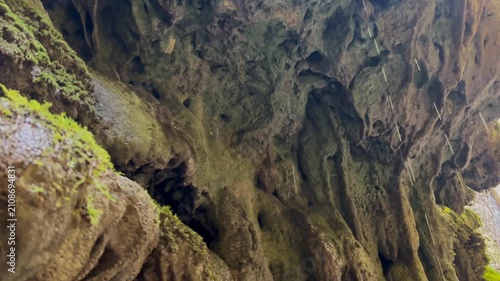 Water drips from the high mossy vault of the cave, creating patterns on the rocks against the background of penetrating light. The concept of the mysterious cave, the power of erosion, wildlife
