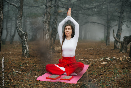 Woman meditating with raised hands in a foggy autumn forest