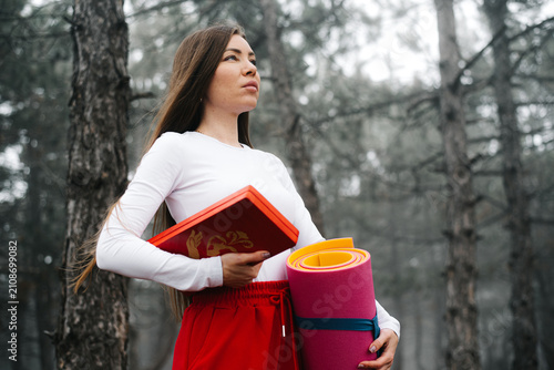 Portrait of a woman holding a yoga mat and sadhu boards in a forest
