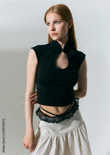 A stylish red-haired woman with big blue eyes poses in summer clothes on a light background