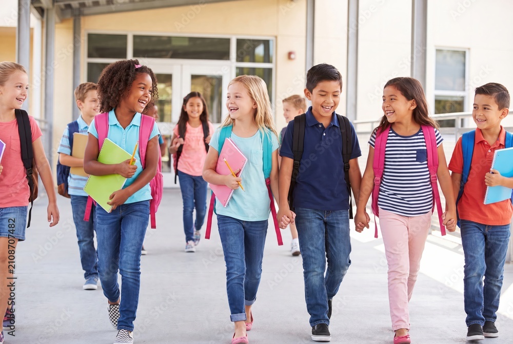 Obraz premium Diverse group of happy elementary school children walking together after school with backpacks and books.