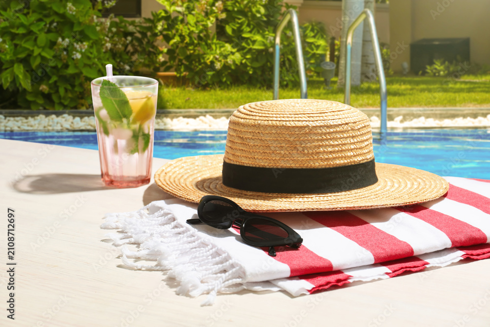 Obraz premium Sunglasses, straw hat, cocktail and towel by swimming pool