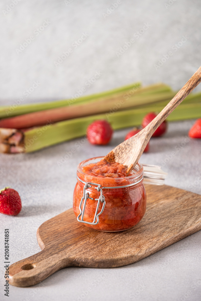 Fototapeta premium Homemade strawberry rhubarb jam in glass jar with wooden spoon