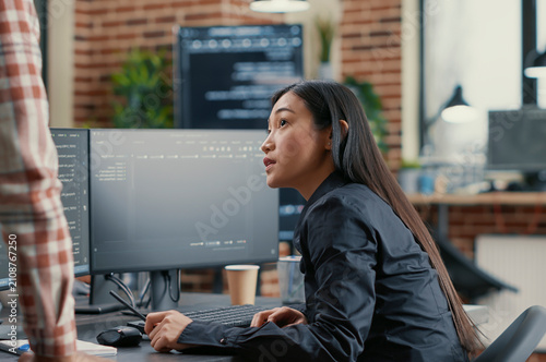 Photos Database developer points a pencil at a computer screen while explaining a compiling algorithm to a coworker during a software team project