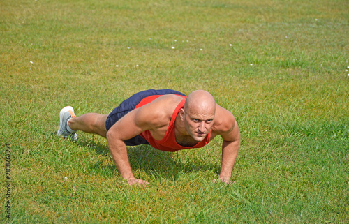 bald male athlete doing push-ups on the green lawn at the stadium. outdoor training. active lifestyle and sports concept