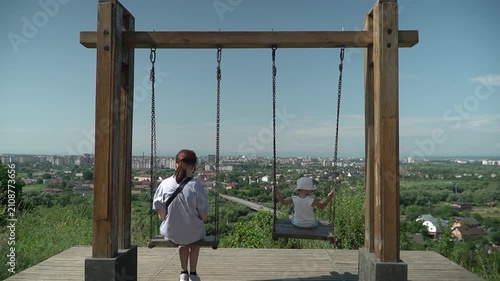 Tourist spot, swing with panoramic view, two girls riding, slow motion, sunny summer day