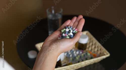 Person pouring medication capsules back into bottle. Close-up view of a person's hands pouring a large handful of colorful pills and capsules back into a white bottle, symbolizing overdose