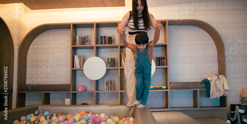 Mother helping her child walk on a soft play structure by a ball pit