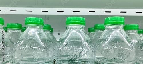 Картината върху платно Clear plastic water bottles with green caps arranged on a white shelf
