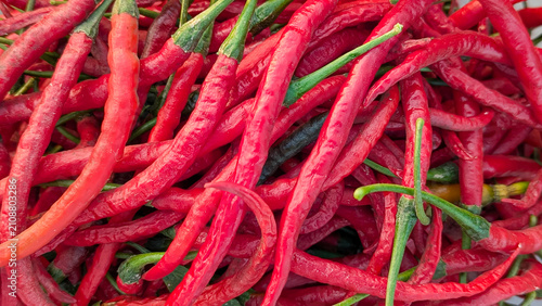 Close up background of fresh long red curly chili peppers with green stems, ideal for cooking, food, and culinary concept.