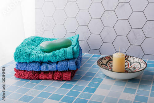 A stack of colorful towels, a bar of soap, and a candle.