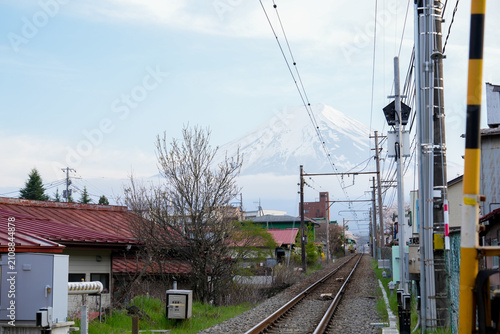 Railway Crossing and Train Tracks Leading toward Mount Fuji Snow Peak in Japan A scenic perspective along a railroad track with a level crossing barrier in a local Japanese town.