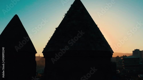 Cinematic silhouette of the historic Üç Kümbetler (Three Tombs) in Erzurum during sunset, featuring a dramatic sunburst and lens flare between the conical roofs.