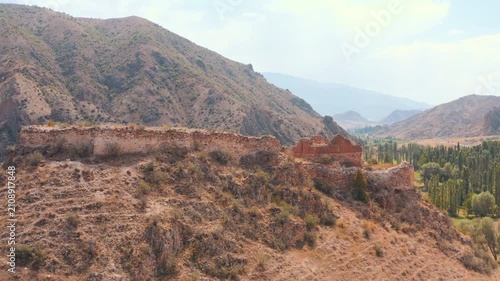 Cinematic aerial drone reveal shot flying over the ancient stone walls of the historic Pernek Castle to unveil a lush green valley and mountains in Oltu, Erzurum.