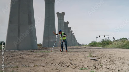 Survey engineer using an automatic level mounted on a tripod to perform elevation measurements during construction of an elevated railway infrastructure project.
